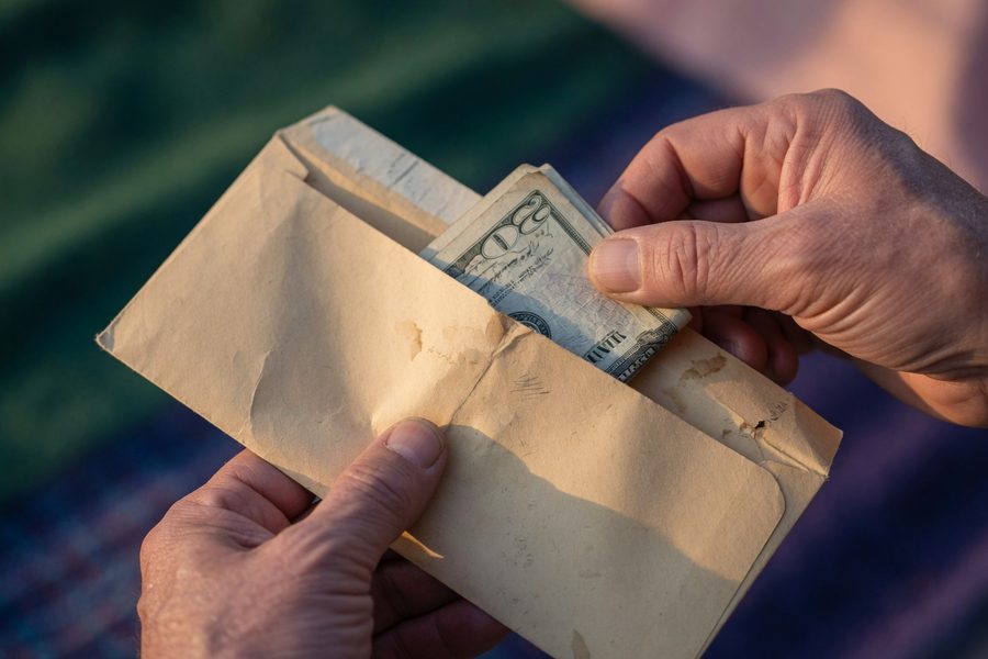 A person sorting dollar bills into labeled paper envelopes on a kitchen table