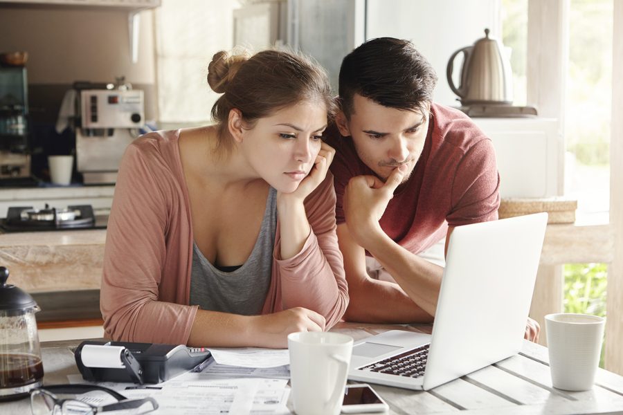 Couple reviewing credit reports on laptop at kitchen table